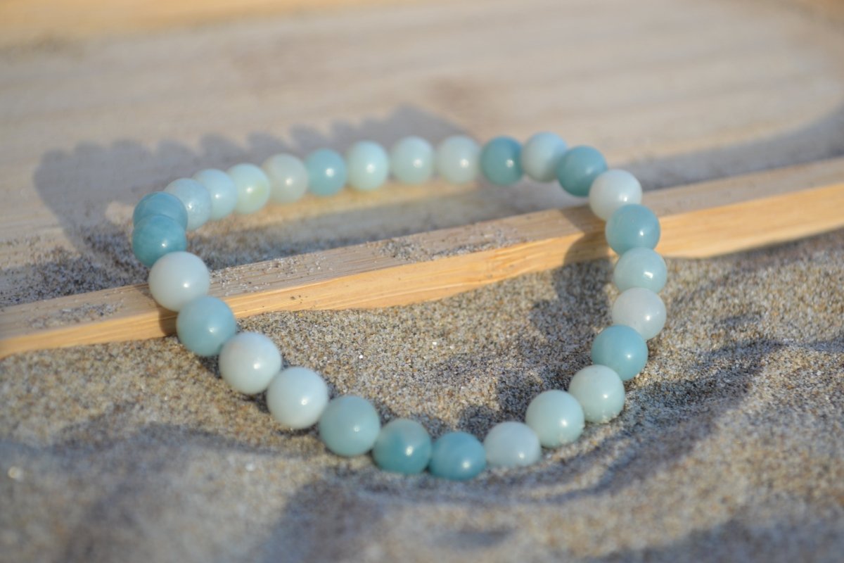 Bracelet Amazonite en pierre naturelle posé sur du sable à cheval sur un plateau en bois. perle de diamètre 5-6mm