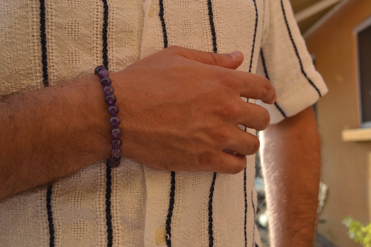 Bracelet Améthyste en pierre naturelle porté sur un poignet d'un homme au niveau du ventre. perle de diamètre 7-8mm