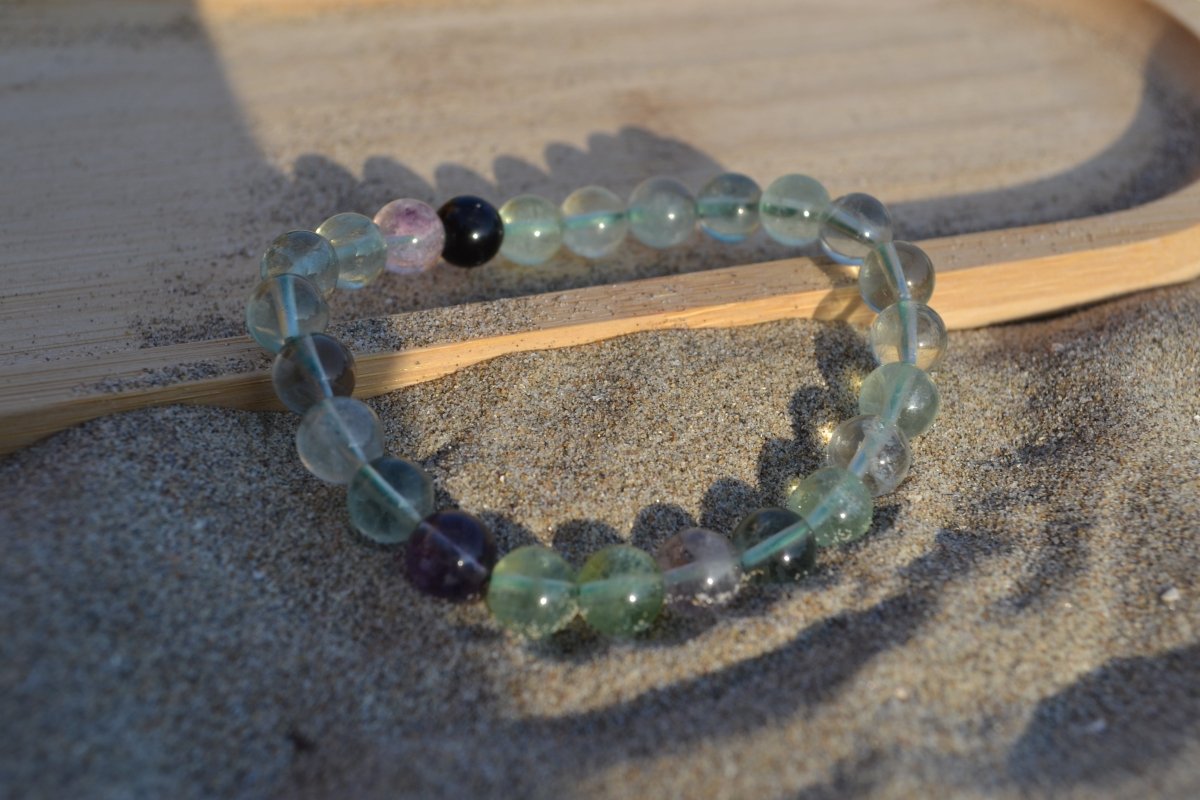 Bracelet Fluorite en pierre naturelle posé sur du sable à cheval sur un plateau en bois. perle de diamètre 7-8mm