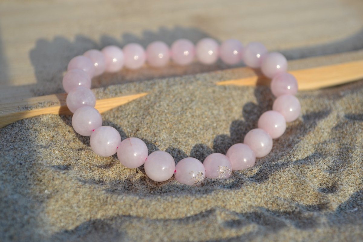 Bracelet Quartz Rose en pierre naturelle posé sur du sable à cheval sur un plateau en bois. perle de diamètre 7-8mm