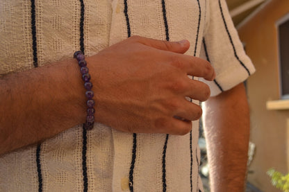 Bracelet Améthyste en pierre naturelle porté sur un poignet d'un homme au niveau du ventre. perle de diamètre 7-8mm